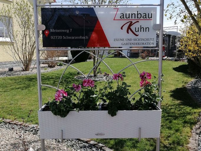 Firmenschild von Zaunbau Kuhn in Schwarzenbach, eingefasst von einem bepflanzten Hochbeet