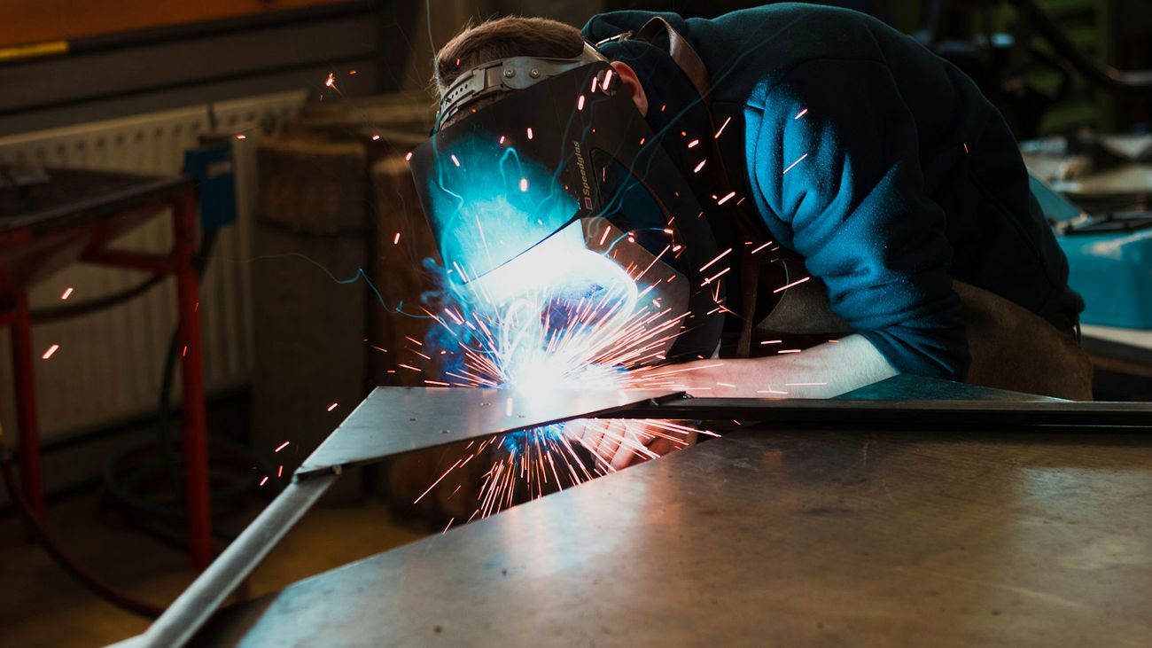 Schweißer bei der Arbeit an einem Stahlbauteil, Funkenflug in der Werkstatt