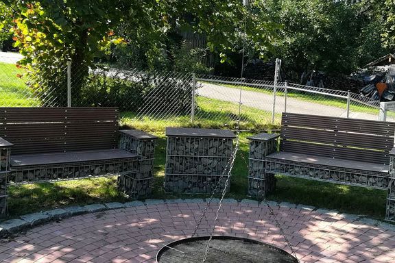 Gabionen mit integrierten Holzbänken rund um einen gepflasterten Sitzplatz im Garten