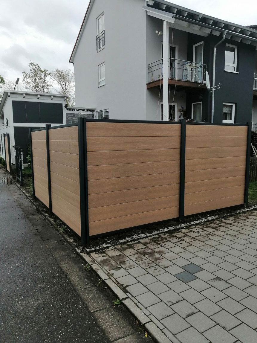 Mülltonnenbox aus WPC in Holzoptik mit Anthrazit-Rahmen an einer Hofeinfahrt
